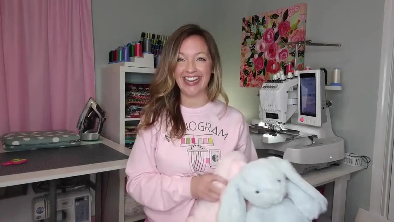 Woman holding two plush bunnies, one pink and one blue, with embroidered ears.