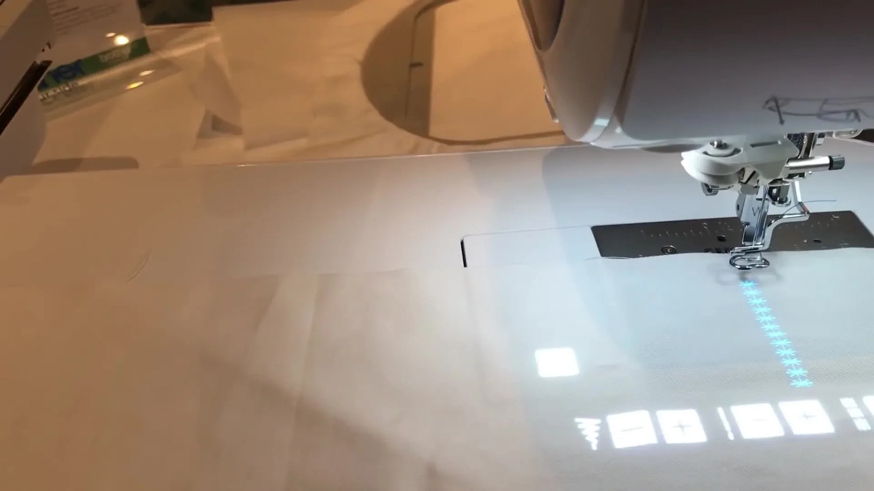 A bright stitch pattern is projected directly onto white fabric, showing how StitchVision preview helps placement before sewing.
