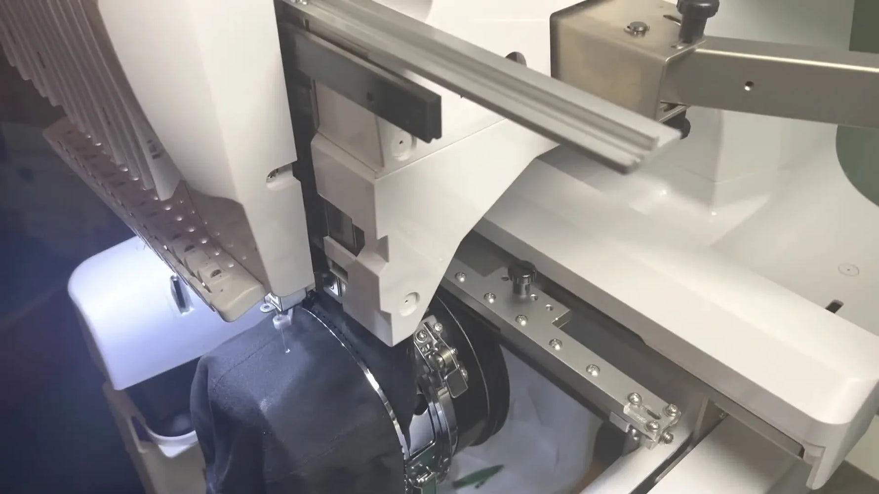 Close-up of a multi-needle machine stitching a white logo onto a black dad hat in cap frame mode.