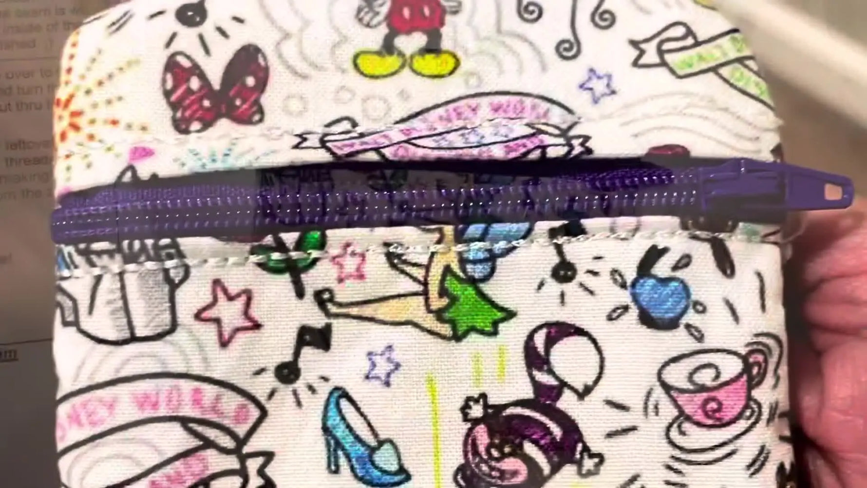 The finished mini zipper pouch is turned right-side out, showing the Disney print fabric and purple zipper in a close-up reveal.