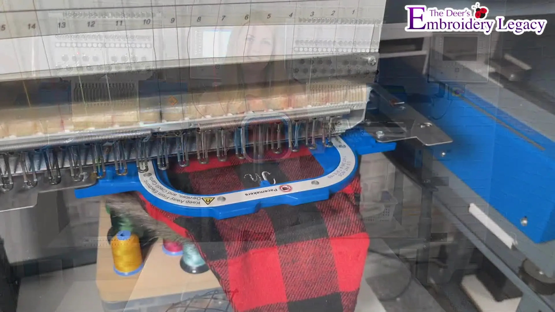 Close-up of a blue magnetic-style hoop mounted on a multi-needle embroidery machine, holding a thick plaid Santa hat for stitching.