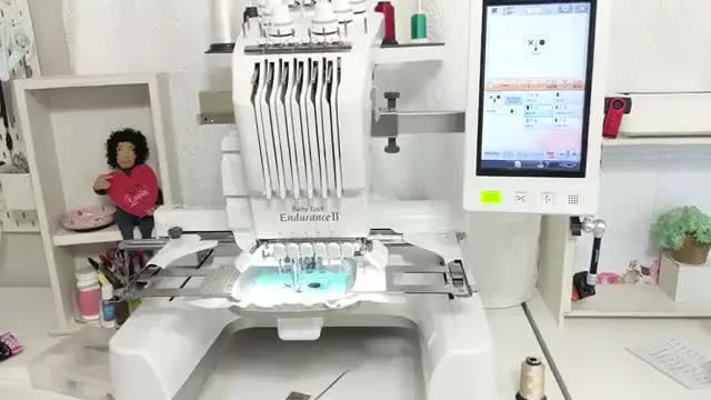 A bright sewing room shot of a Baby Lock Endurance II 6-needle embroidery machine, representing metered tension systems that self-adjust during stitching.
