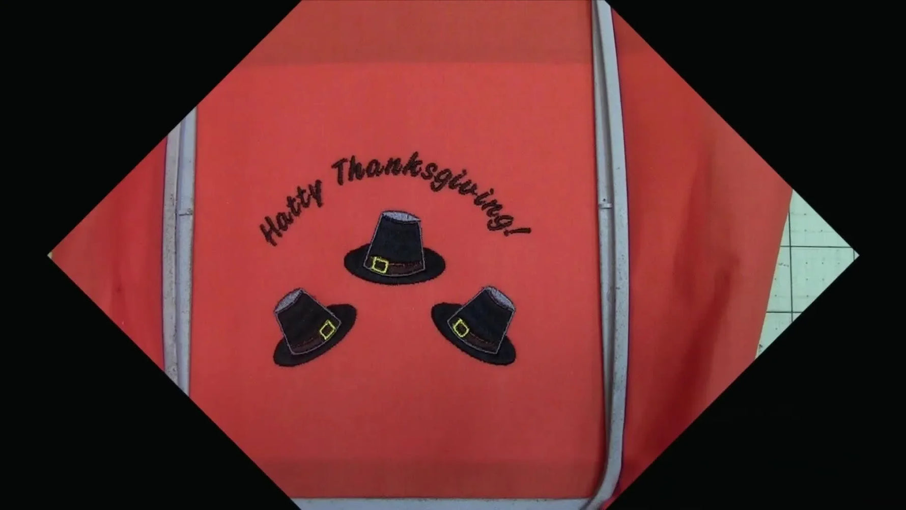 Close-up of final stitch-out: three pilgrim hats and curved text on orange fabric.