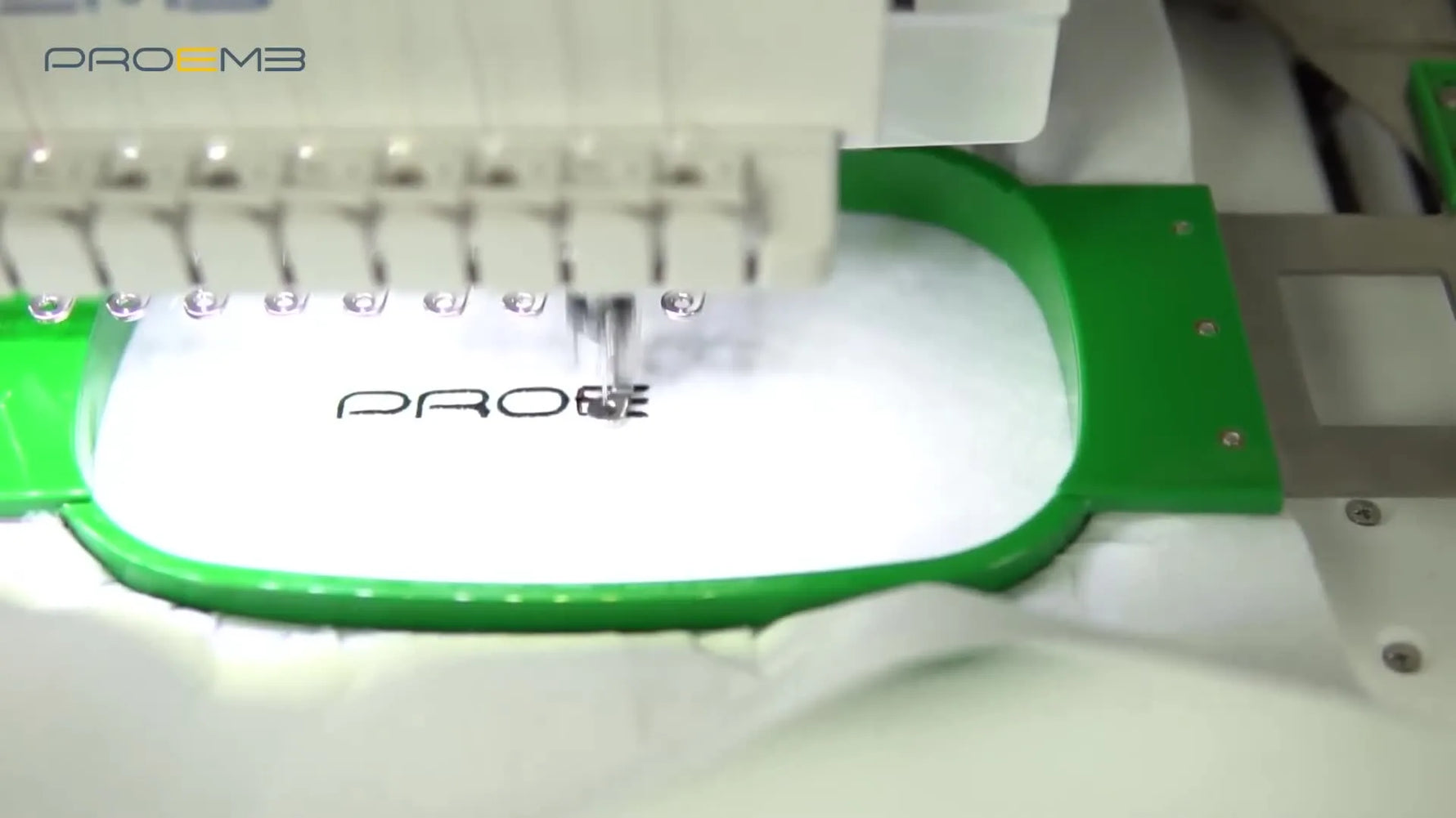 A close-up of the BF1500 needle stitching the PROEMB logo on white fabric held in a green tubular hoop.