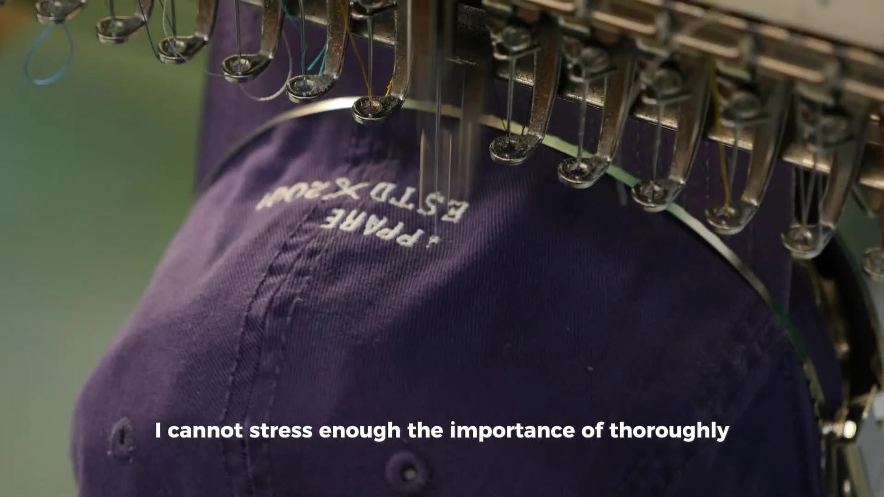 A purple cap mounted on a cap driver is being embroidered with a white logo, showing a clean, production-ready cap setup.