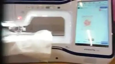 The Brother Innov-is XV screen shows a scanned hoop background with a flower design overlay, making precise placement inside a stitched border easy to verify before stitching.