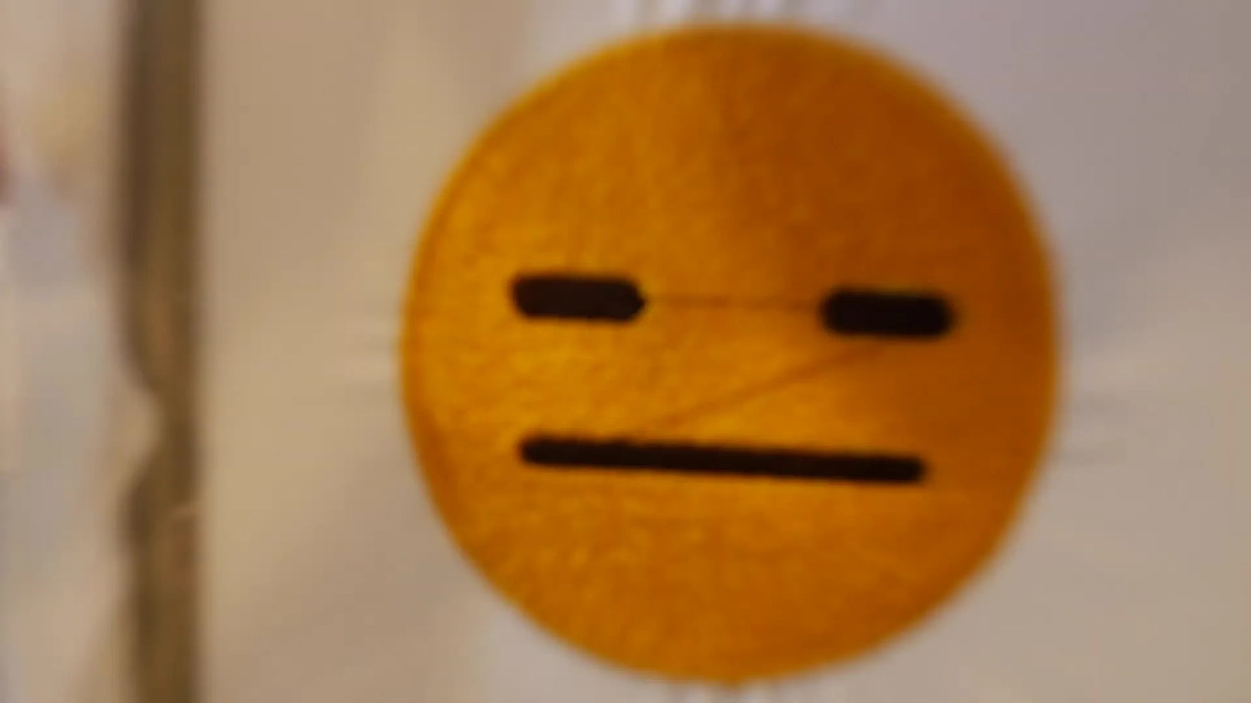 The finished sarcastic emoji embroidery is shown in the hoop, with a gold face and dark brown details ready for patch finishing.