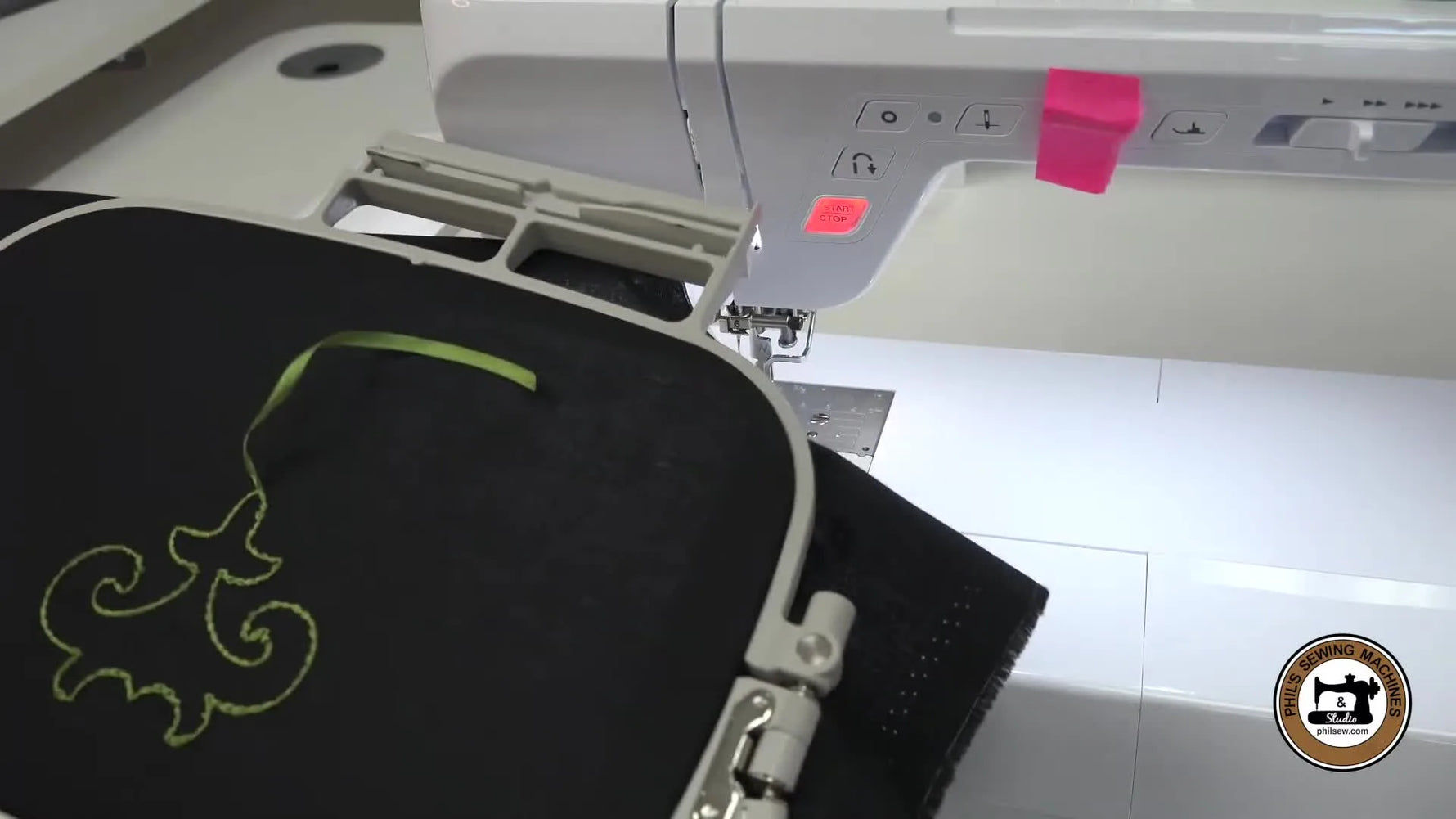 The hoop is flipped to reveal a finished green ribbon bobbin-work design that looks like hand stitching on black fabric.