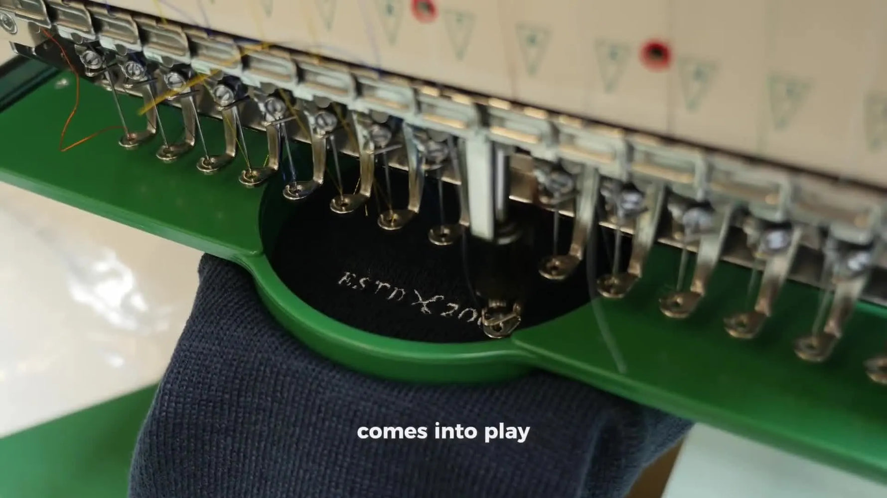 A close-up of a commercial embroidery machine stitching a logo in a green hoop, capturing the speed and consistency that pre-wound bobbins support.