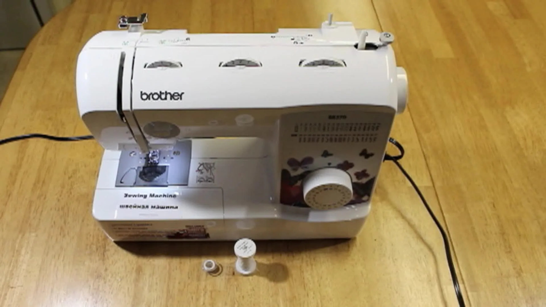 Brother sewing machine on a wooden table with a bobbin and thread spool in the foreground.