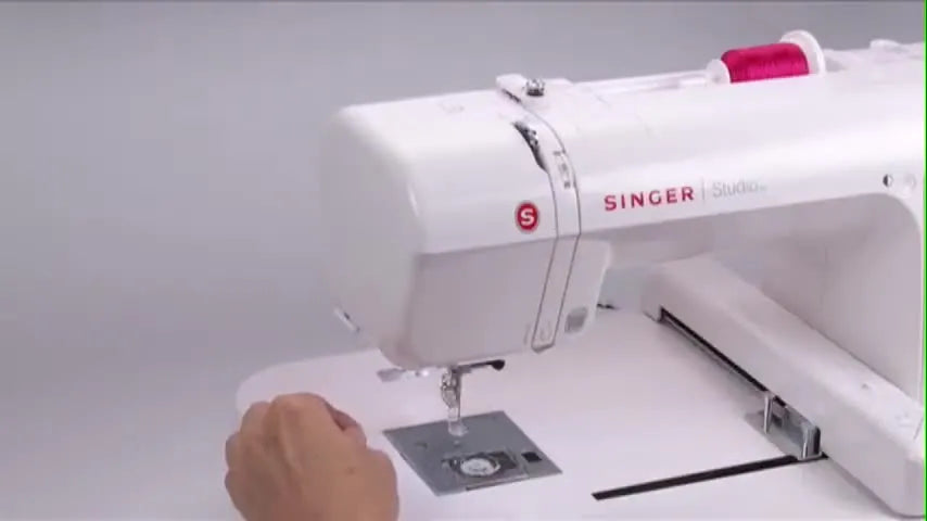A close-up shows the upper thread being pulled with the presser foot down to confirm proper tension-disc engagement on a Singer Studio embroidery machine.