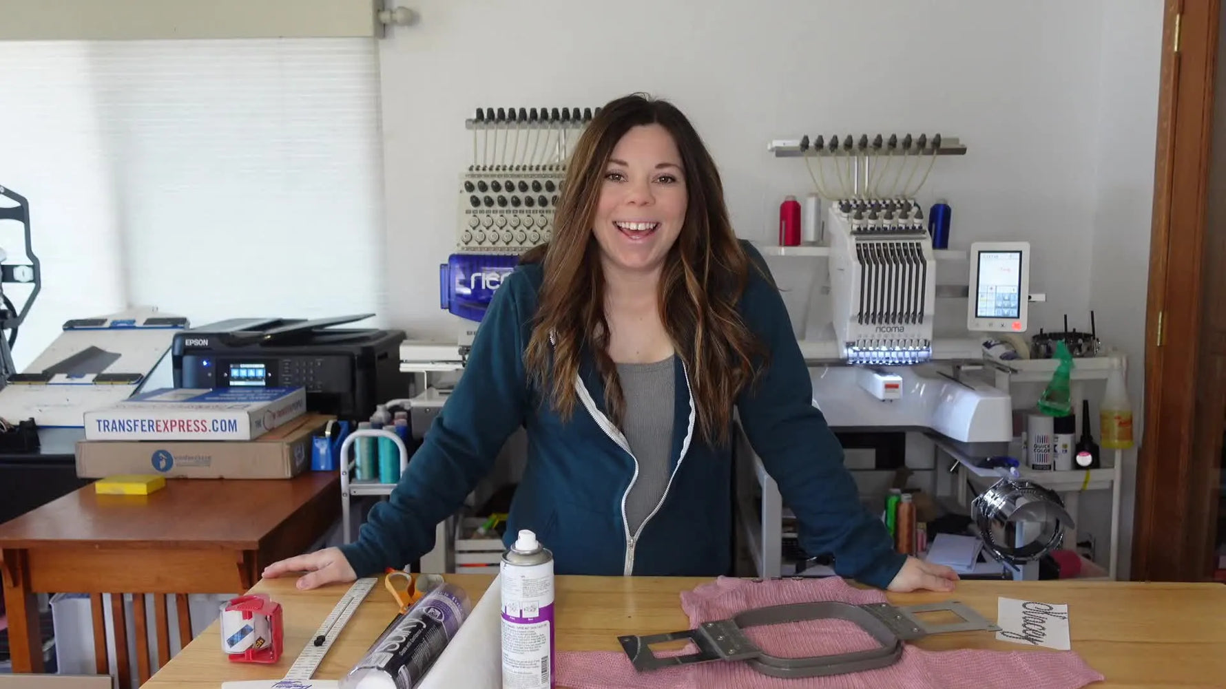Woman introduces the knit baby onesie and embroidery supplies with the machine in the background.