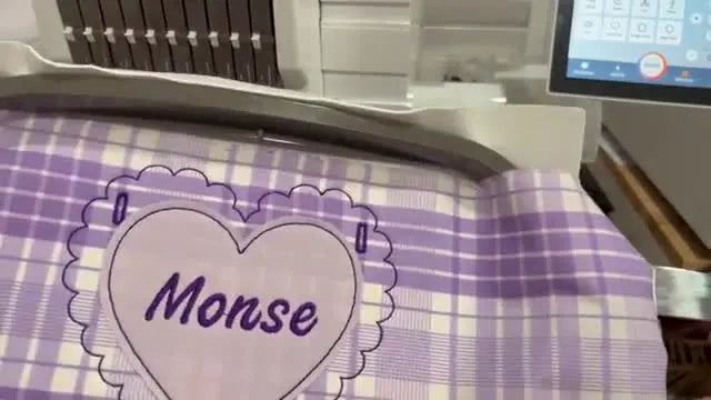 A close-up of the finished personalized heart appliqué still in the hoop, showing clean satin borders and crisp fabric placement.