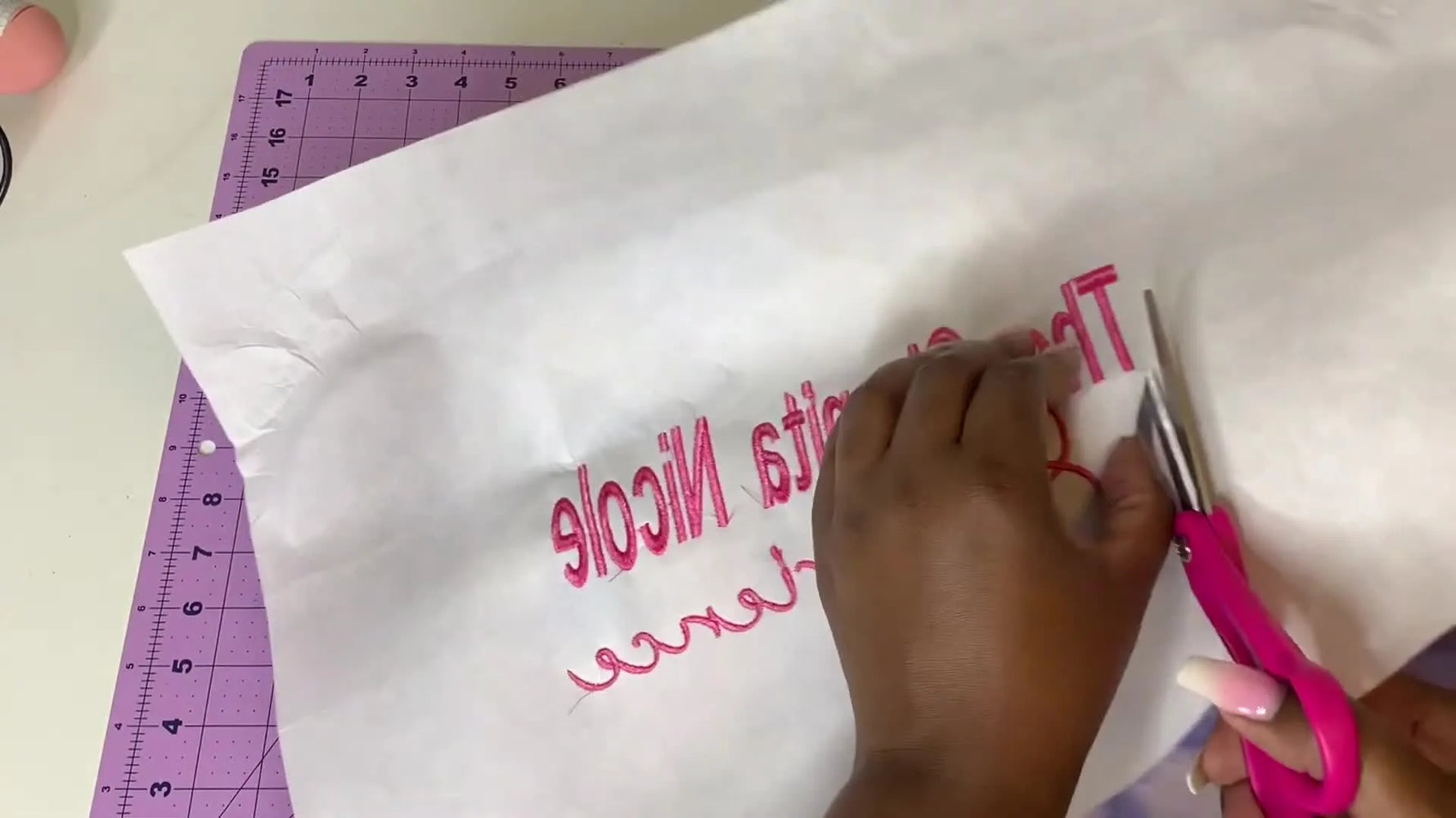 The finished pink text embroidery revealed on a tie-dye crop top sweater after stitching on a Ricoma EM1010.