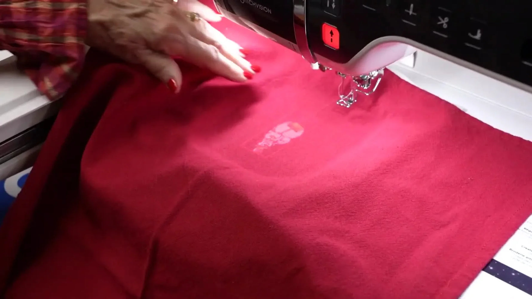 The Brother Aveneer projector casts the snowman design onto a red kitchen towel so you can nudge placement before stitching.