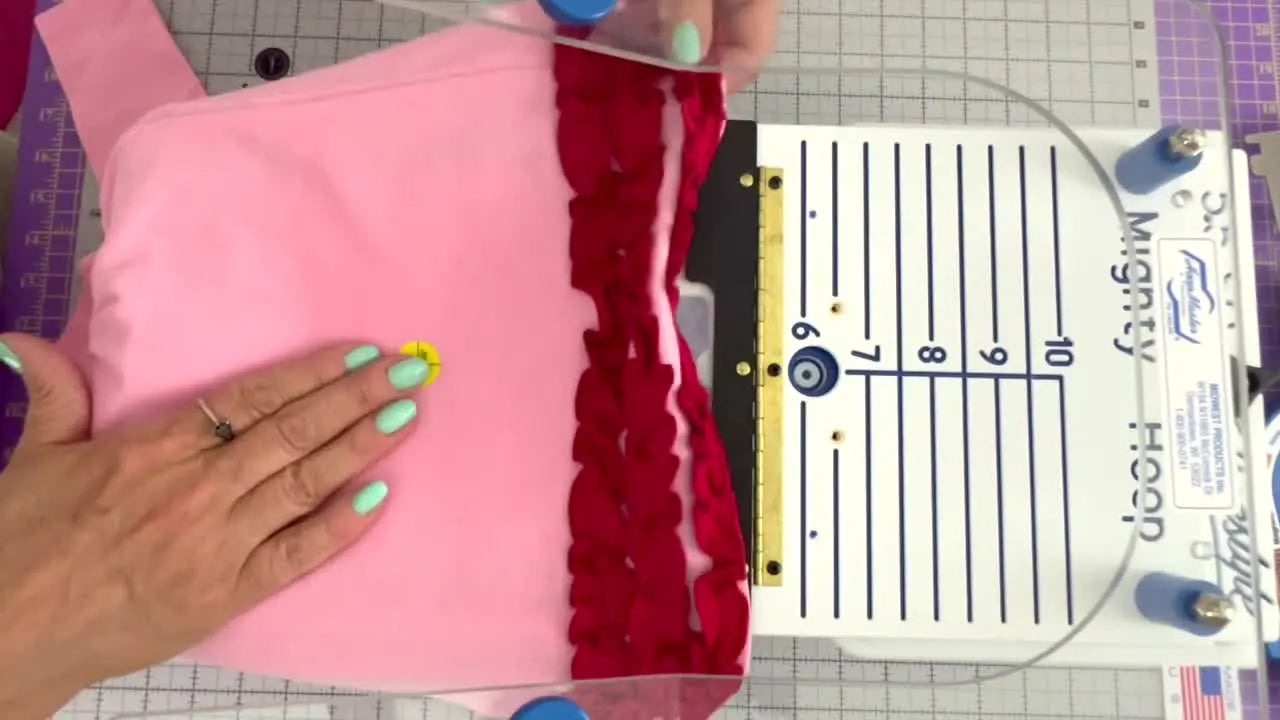A knit dress is aligned on a hooping station so the target sticker crosshair sits precisely on the station’s zero mark before snapping on the magnetic hoop.