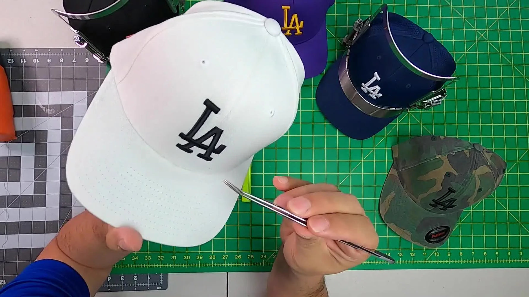 An overhead shot of a heat gun being waved over a finished 3D puff logo on a black cap to shrink tiny foam specks for a crisp, retail-ready look.
