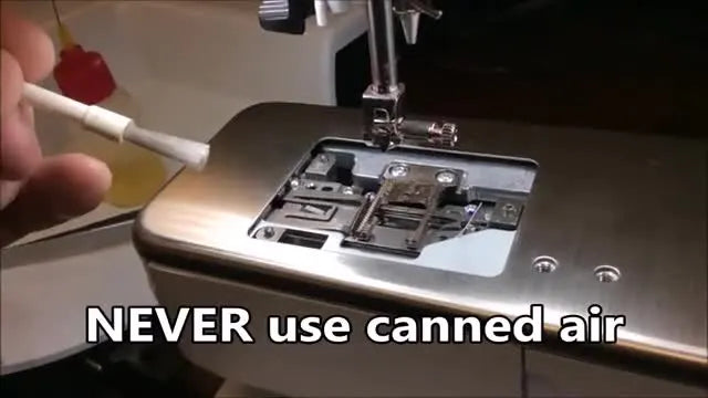 A small white brush gently sweeping lint out of the exposed thread catcher mechanism.