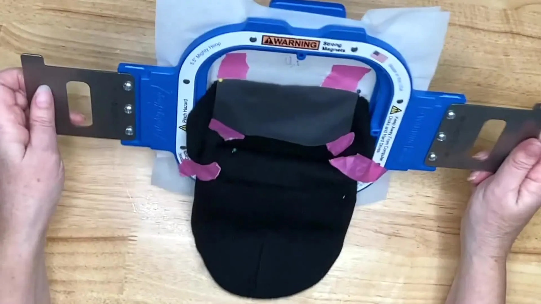 A fully prepped child’s beanie is floated onto hooped stabilizer inside a magnetic hoop, secured with pins, painter’s tape, and a water-soluble topper, ready to stitch.