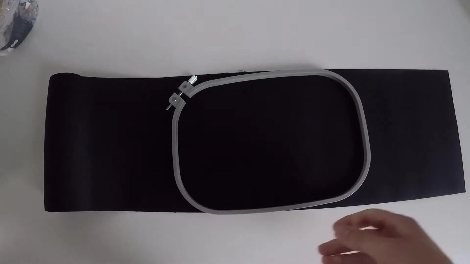 Hands holding the top and bottom parts of a magnetic embroidery frame over black fabric right before the magnets snap together.