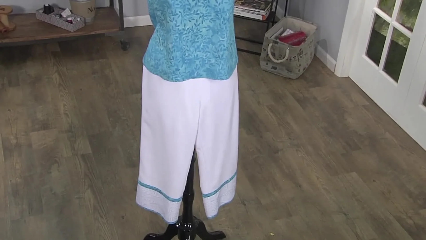 White crop pants on a mannequin featuring a blue embroidered hem band with a clean, boutique-style finish.