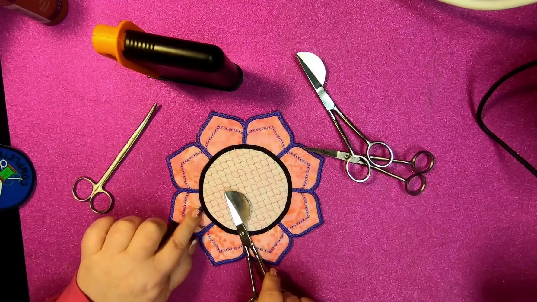Close-up of duckbill scissors held flat against the stabilizer while trimming appliqué fabric safely inside the hoop.