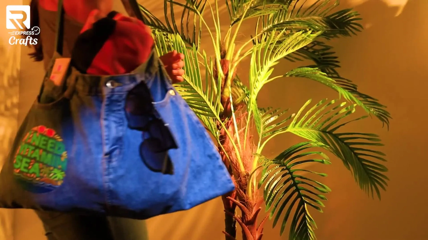 A finished denim beach bag made from a jean skirt, featuring a summer-themed embroidery design and sturdy denim handles, styled with a towel and sunglasses.