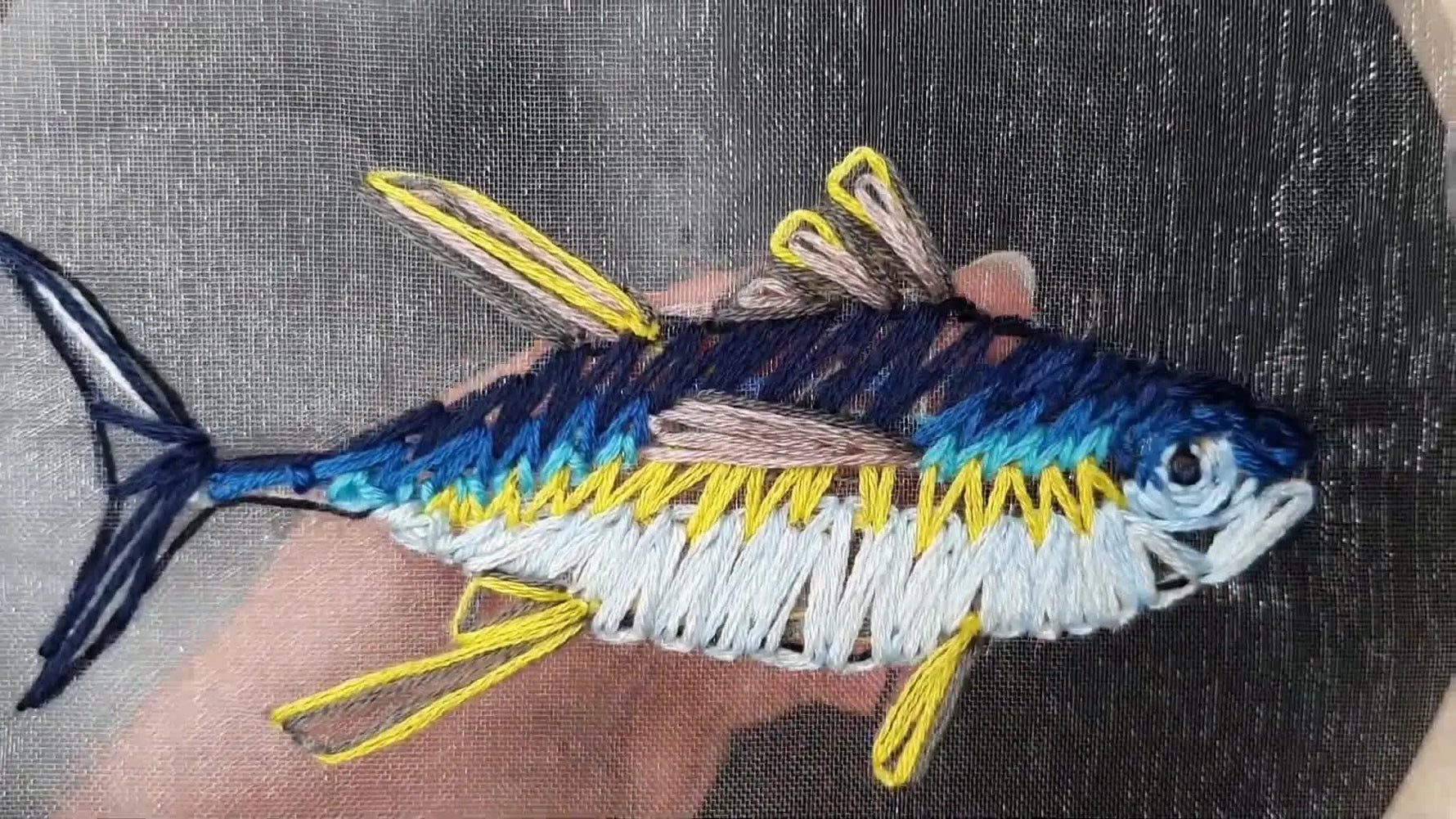 Finished hand-embroidered tuna fish on sheer fabric.
