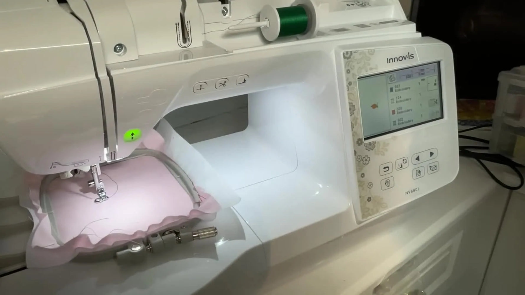 The Brother Innov-is 880E stitches a rose design on pink fabric with the start button lit, showing the machine in active embroidery mode.