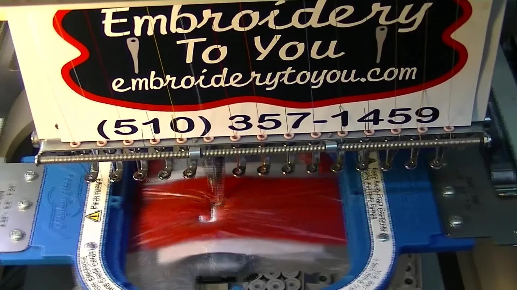 An extreme close-up of white lettering being stitched into a red terry cloth sweatband under a presser foot, showing how topping prevents stitches from sinking.