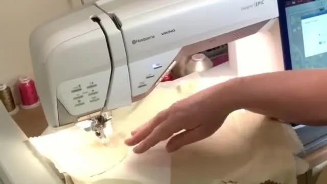 Hands gently smooth silk patches near the needle while the Husqvarna Viking Designer EPIC stitches, using foot-pedal speed control for precision.