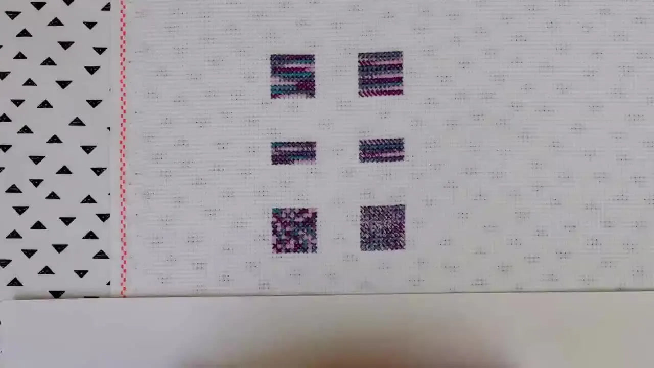Overhead shot of white Aida fabric with six small stitched squares, and hands framing the bottom.