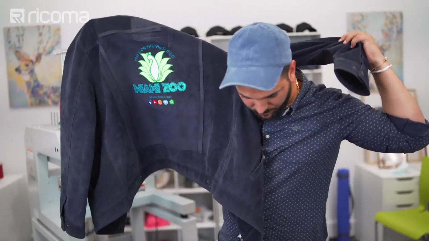 The instructor holds up a finished black denim jacket featuring a colorful multi-layer appliqué design.