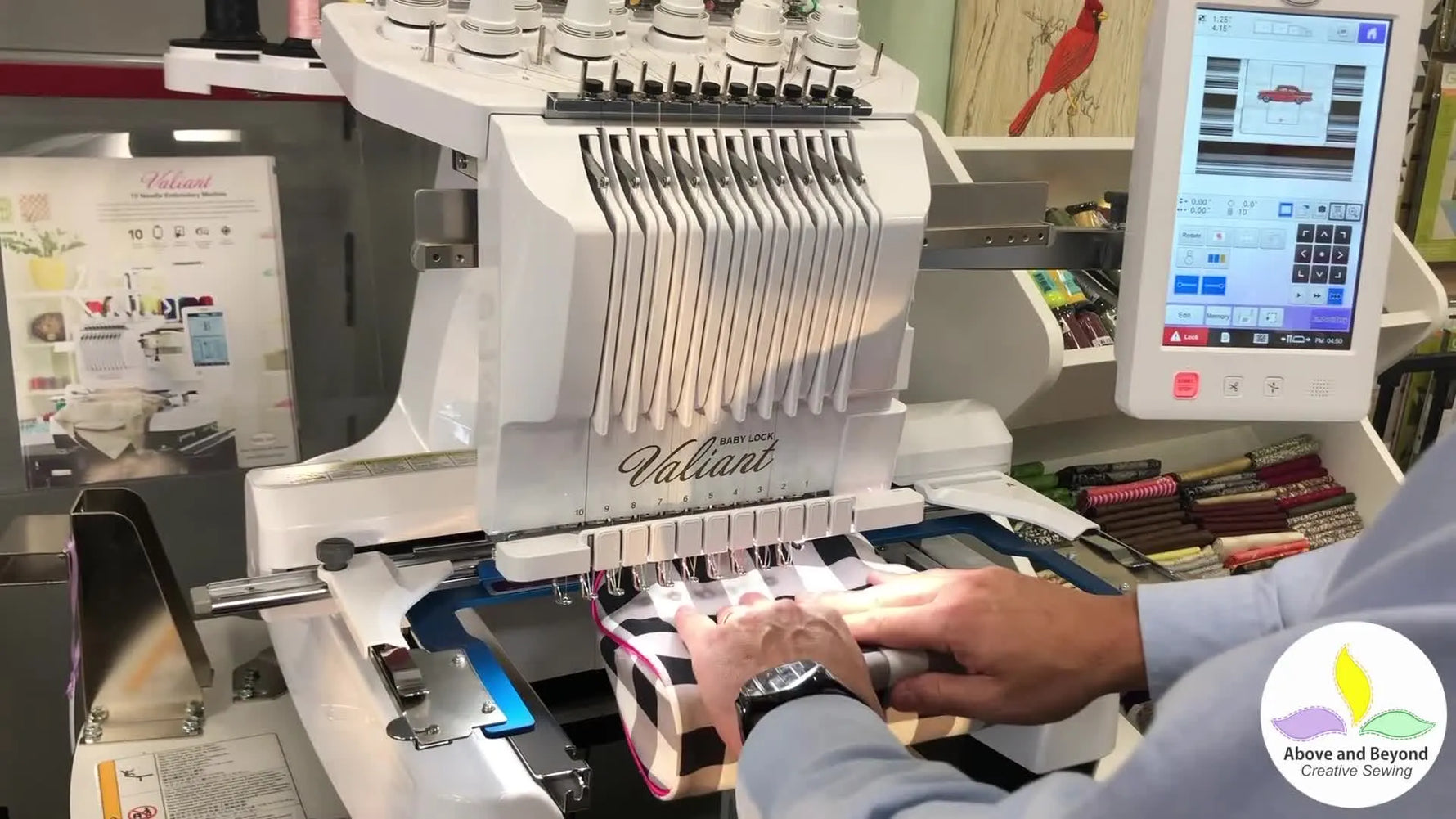 Hands press a small check-patterned purse firmly onto a sticky stabilizer window mounted in a free-arm frame for embroidery.