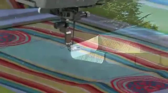 The Janome MC15000 stitches an embroidery design on a large striped fabric piece held in a rectangular hoop.