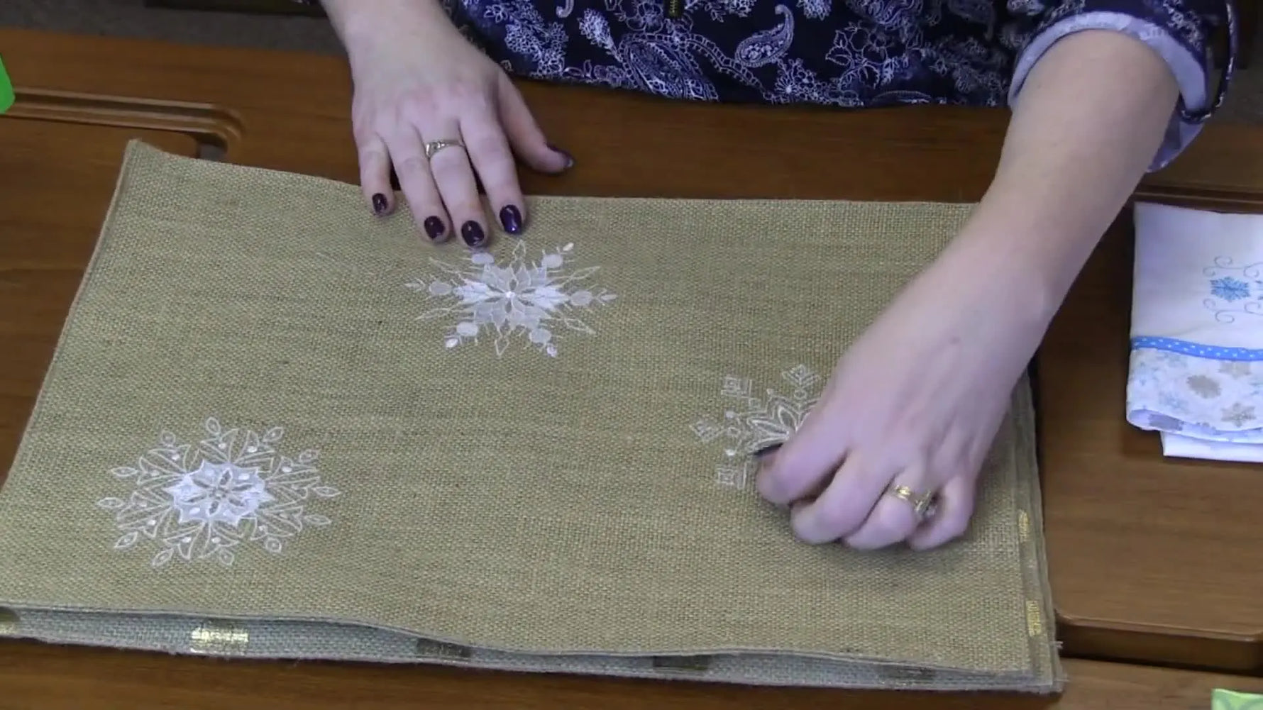 Four burlap-style placemats laid out on a table, each stitched with a bold snowflake design for a winter tablescape.