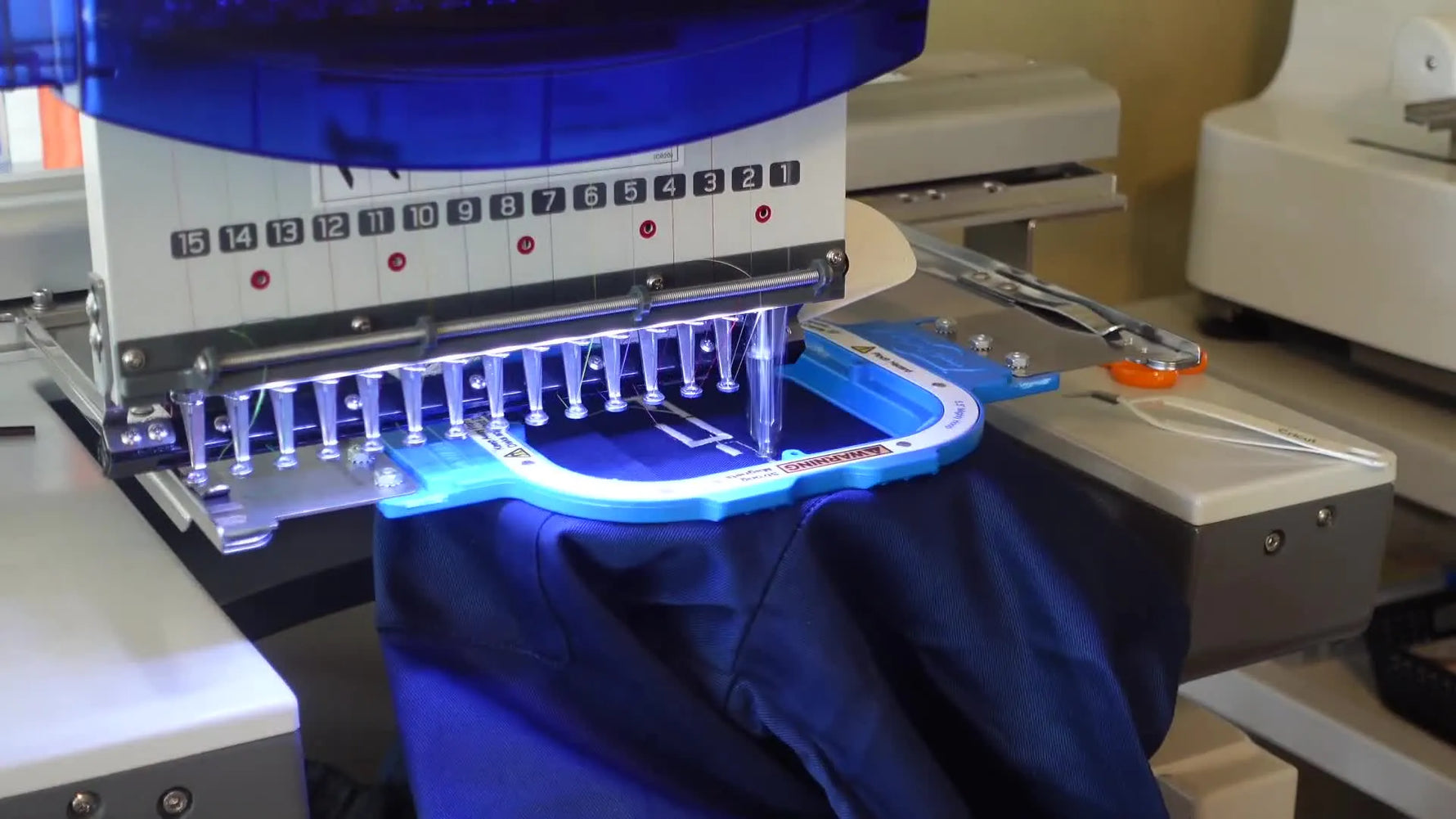 Close-up of a Ricoma machine stitching a white 'F' character onto a navy blue t-shirt.