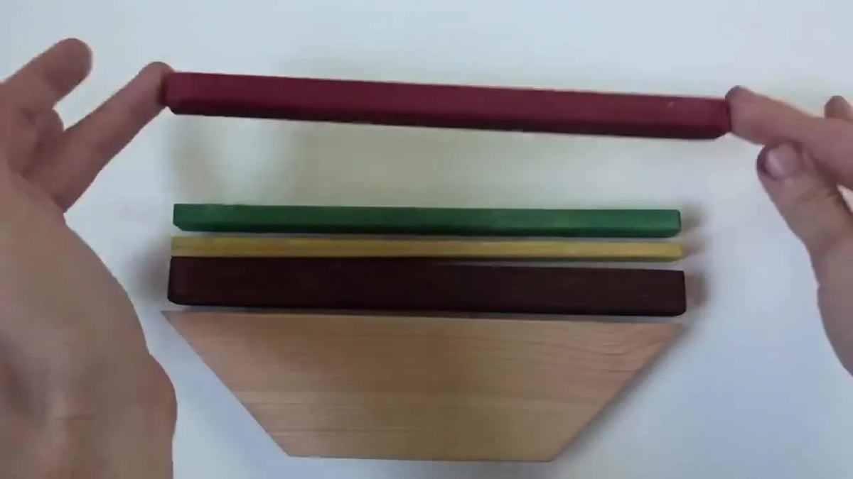 Hands assembling a multi-colored wooden cheeseburger from individually stained wood pieces.