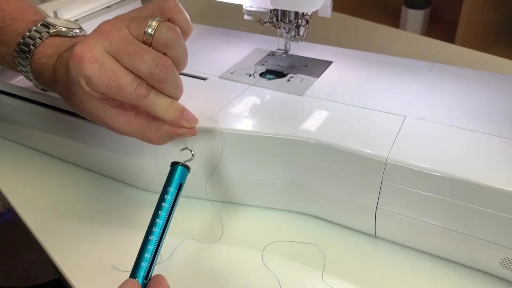 A close-up of the Echidna spring tension gauge hooked into a loop of bobbin thread, ready to measure bobbin tension in grams.