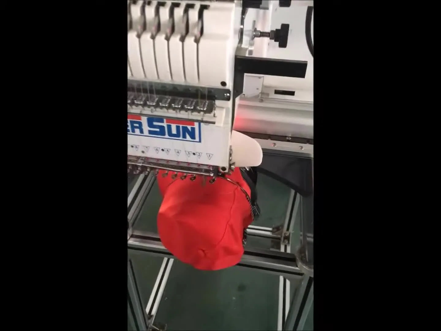 Close-up of the SMX-1501/CP stitching a logo on a rotating red cap mounted on the cap driver.