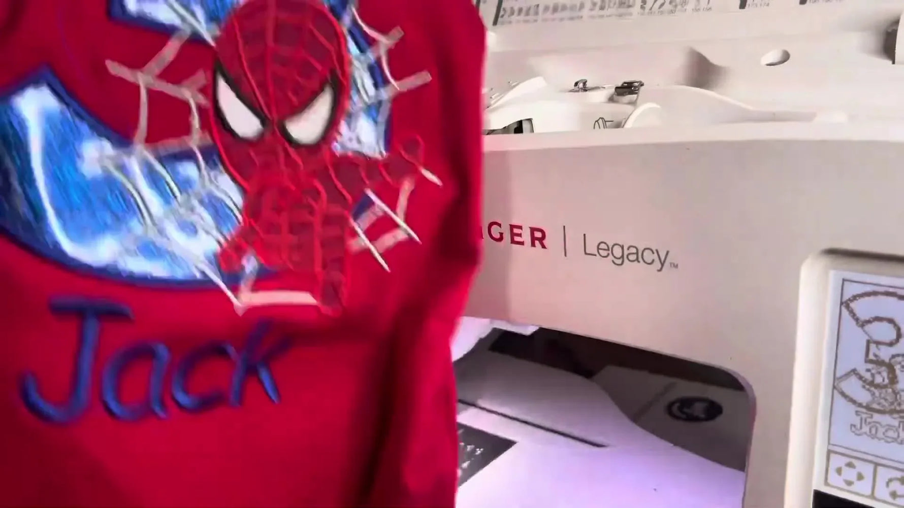 A finished red shirt featuring a blue glitter Spiderman number “3” and the name “Jack,” stitched in-the-hoop on a Singer Legacy SE300.