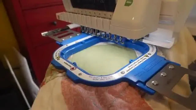 The Brother multi-needle machine begins stitching pink lettering onto a quilt top held securely in a magnetic hoop.
