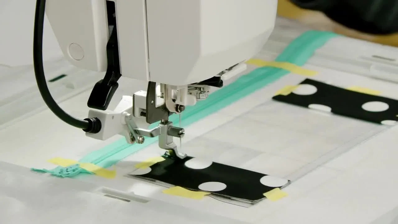 An extreme close-up shows the needle forming a double top-stitch through the vinyl-and-fabric window frame inside the hoop.