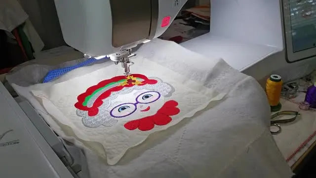 The finished Mrs. Claus quilt block is held up to the camera, showing the curly hair texture, glasses, and holly details.