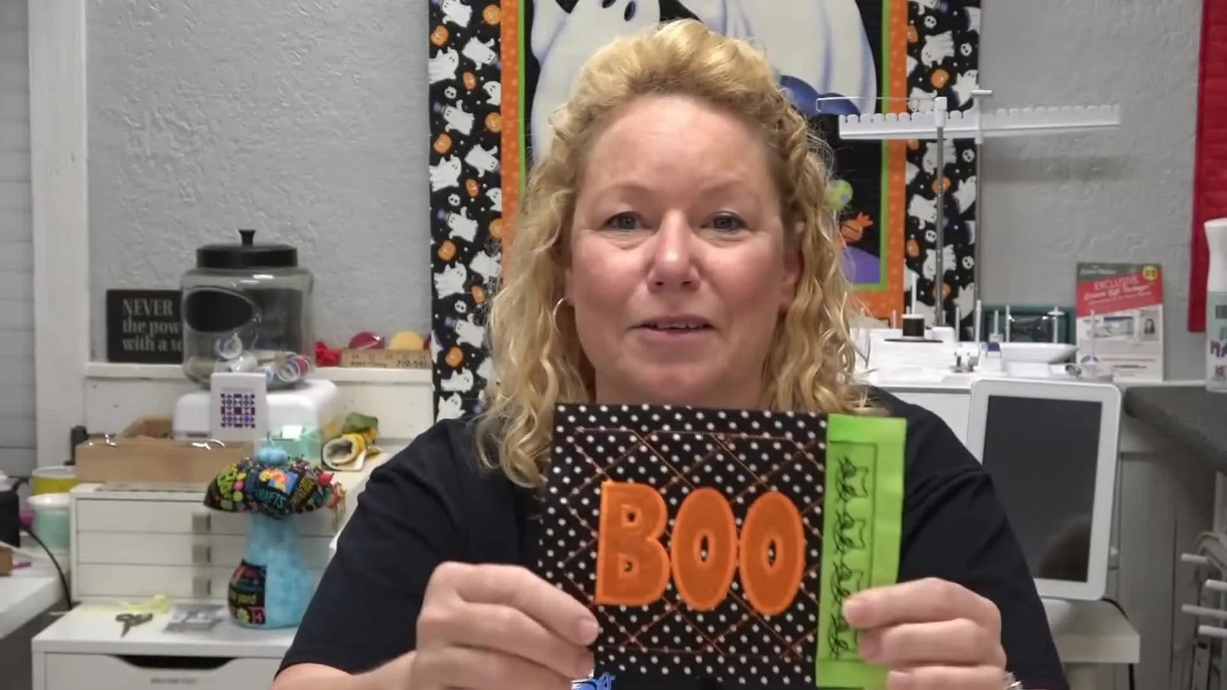 A finished Boo Block is held up to show crisp BOO appliqué letters, cross-hatch quilting, and the cat motif border.