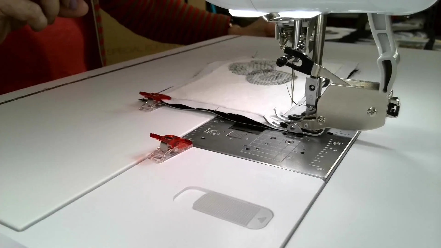 A close-up of the sewing area shows a walking foot stitching black quilt blocks while a green laser guide projects a straight seam line.