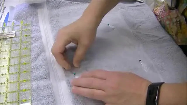 A bath towel is pressed onto sticky wash-away stabilizer inside an embroidery hoop, demonstrating the floating technique that prevents hoop burn.