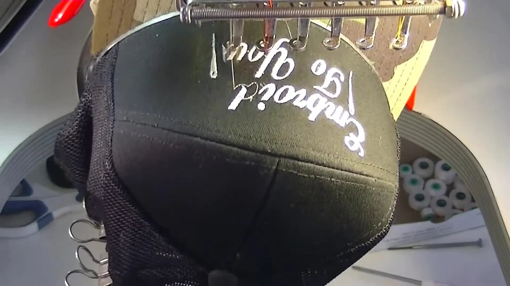 A close-up of a commercial embroidery machine stitching arched cap text at 700 RPM on a 7-panel structured cap.