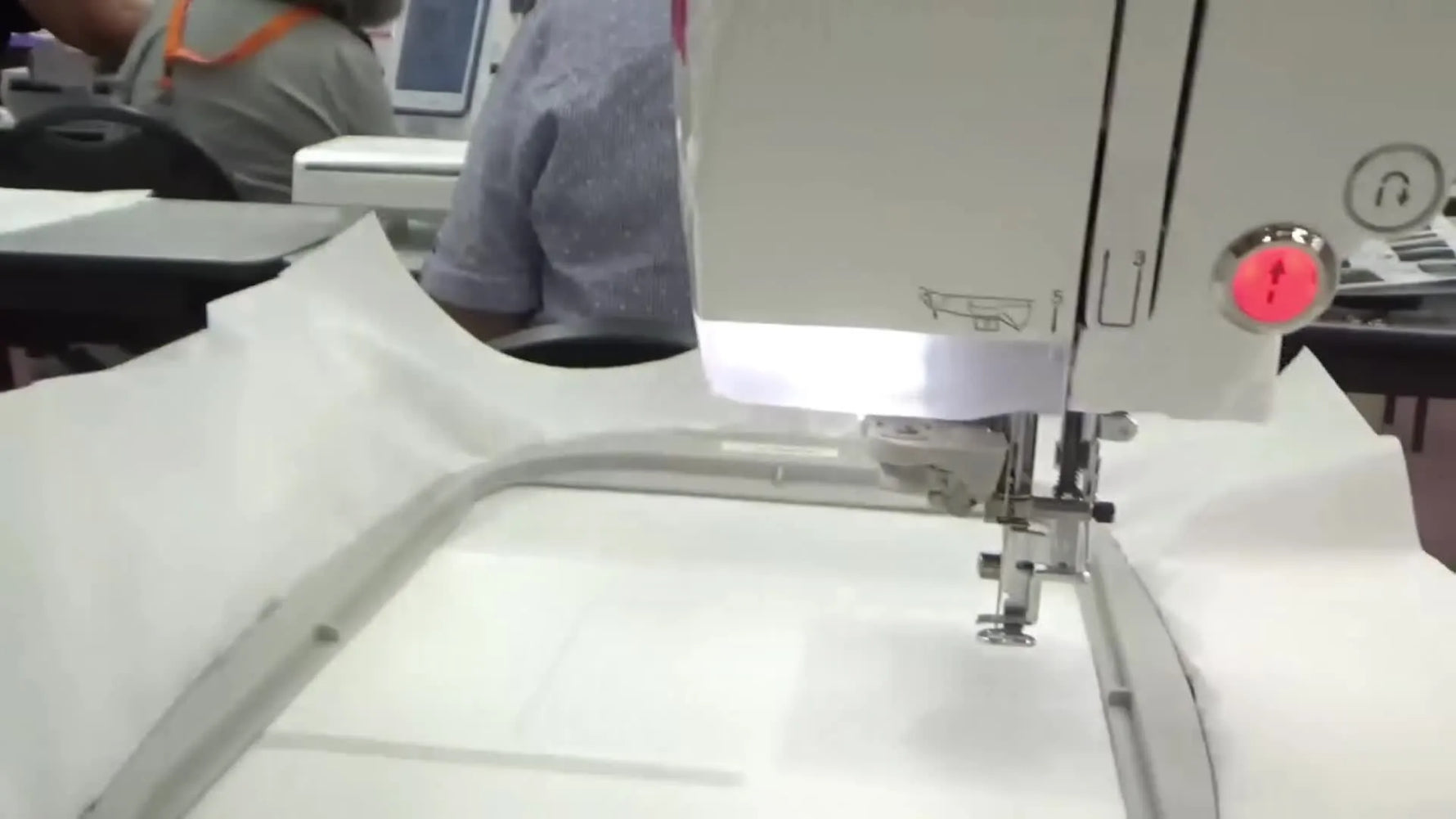 A close-up of an embroidery machine needle hovering over a hooped stabilizer, right before stitching begins.