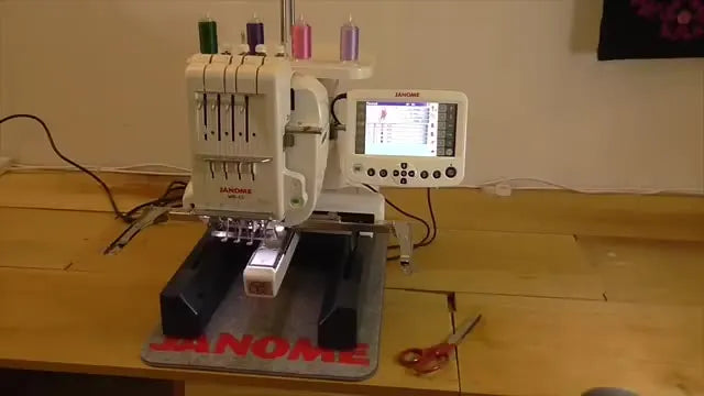A 4-needle Janome MB-4S stitches a design on a black garment while the remote screen and thread stand are visible, signaling a jump from hobby workflow to production workflow.